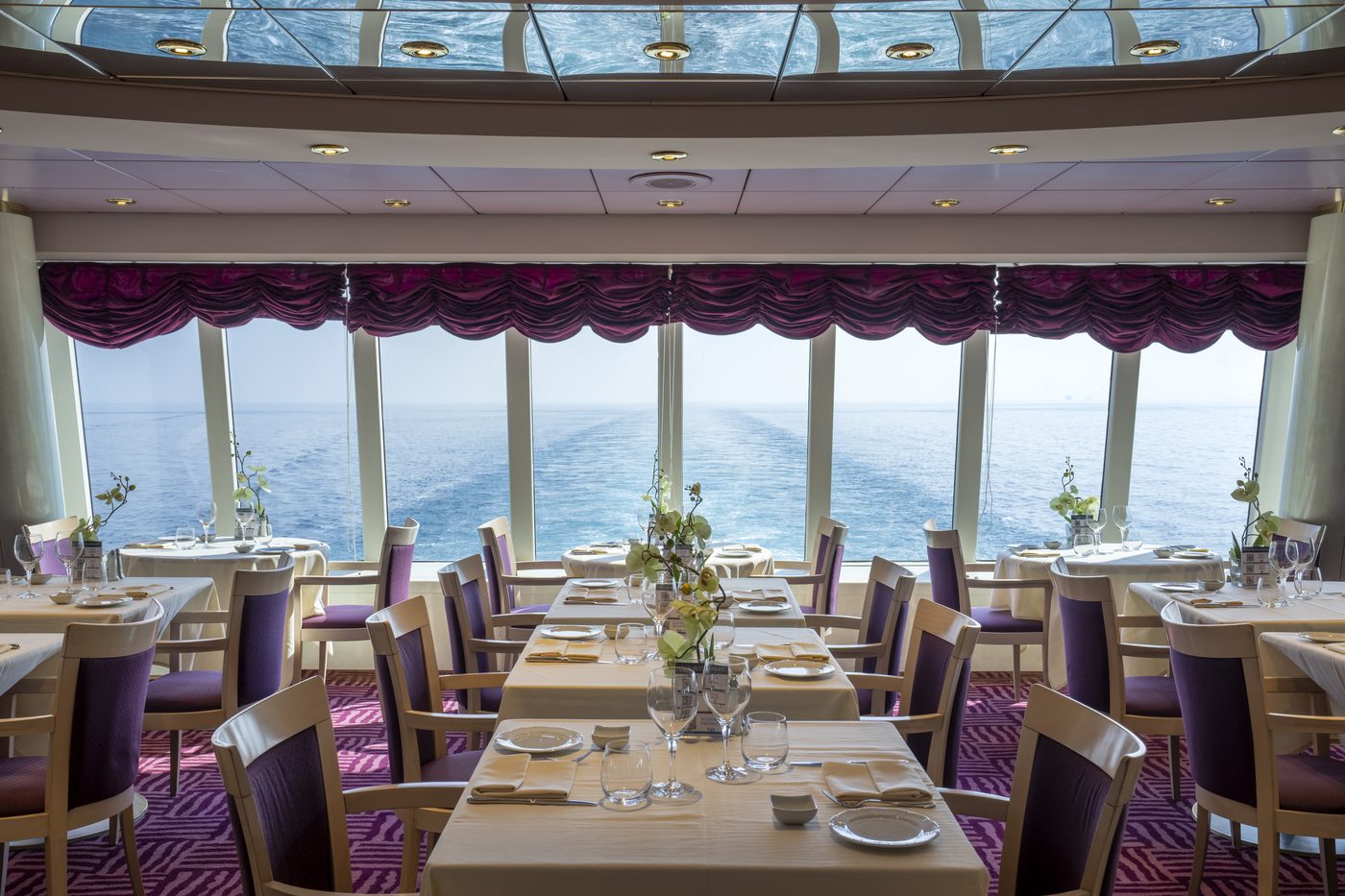 Elegantes Hauptrestaurant an Bord mit eingedeckten Tischen und Panoramafenstern zum Heck