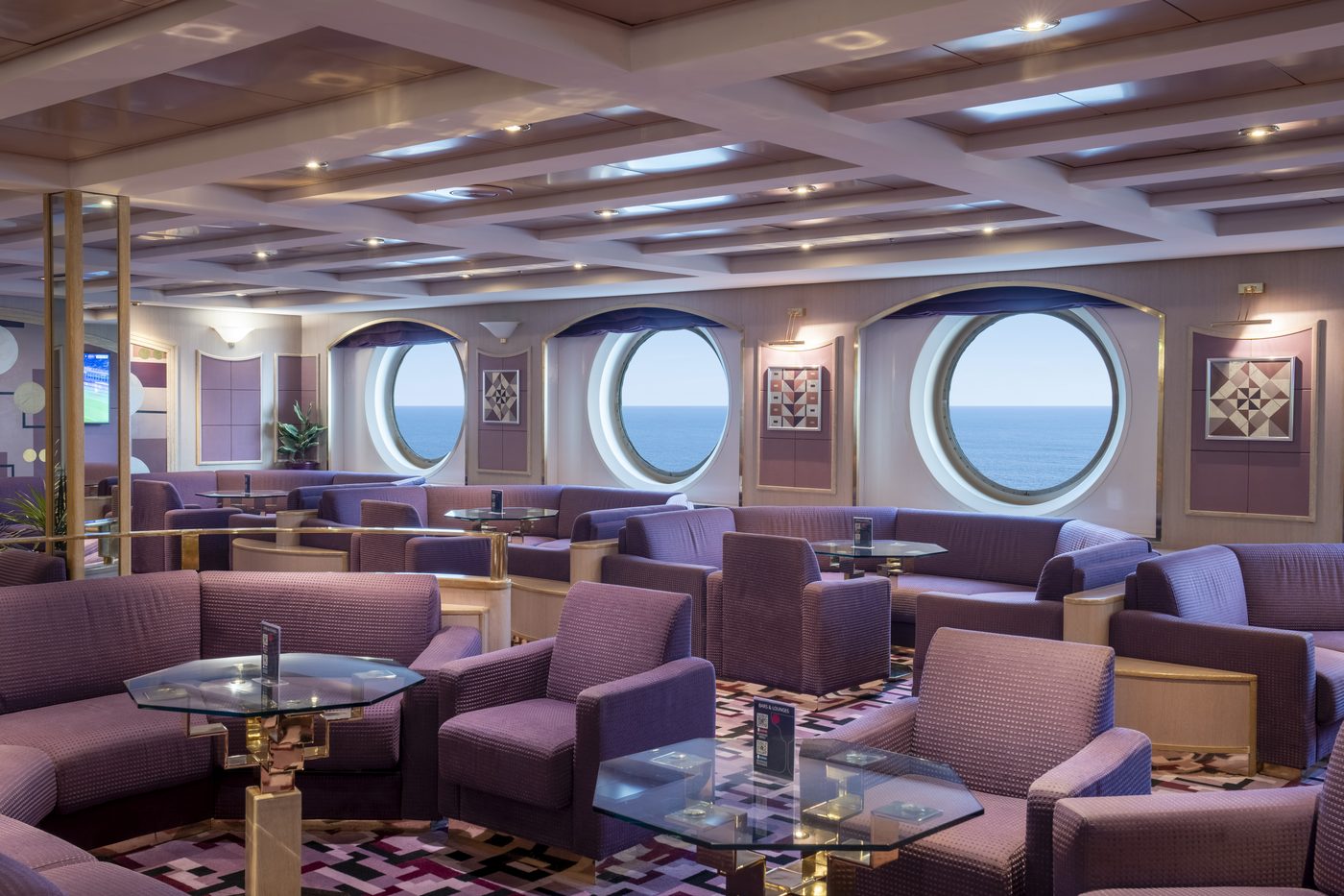 Lounge an Bord mit runden Panoramafenstern, violetten Sesseln und Blick aufs Meer