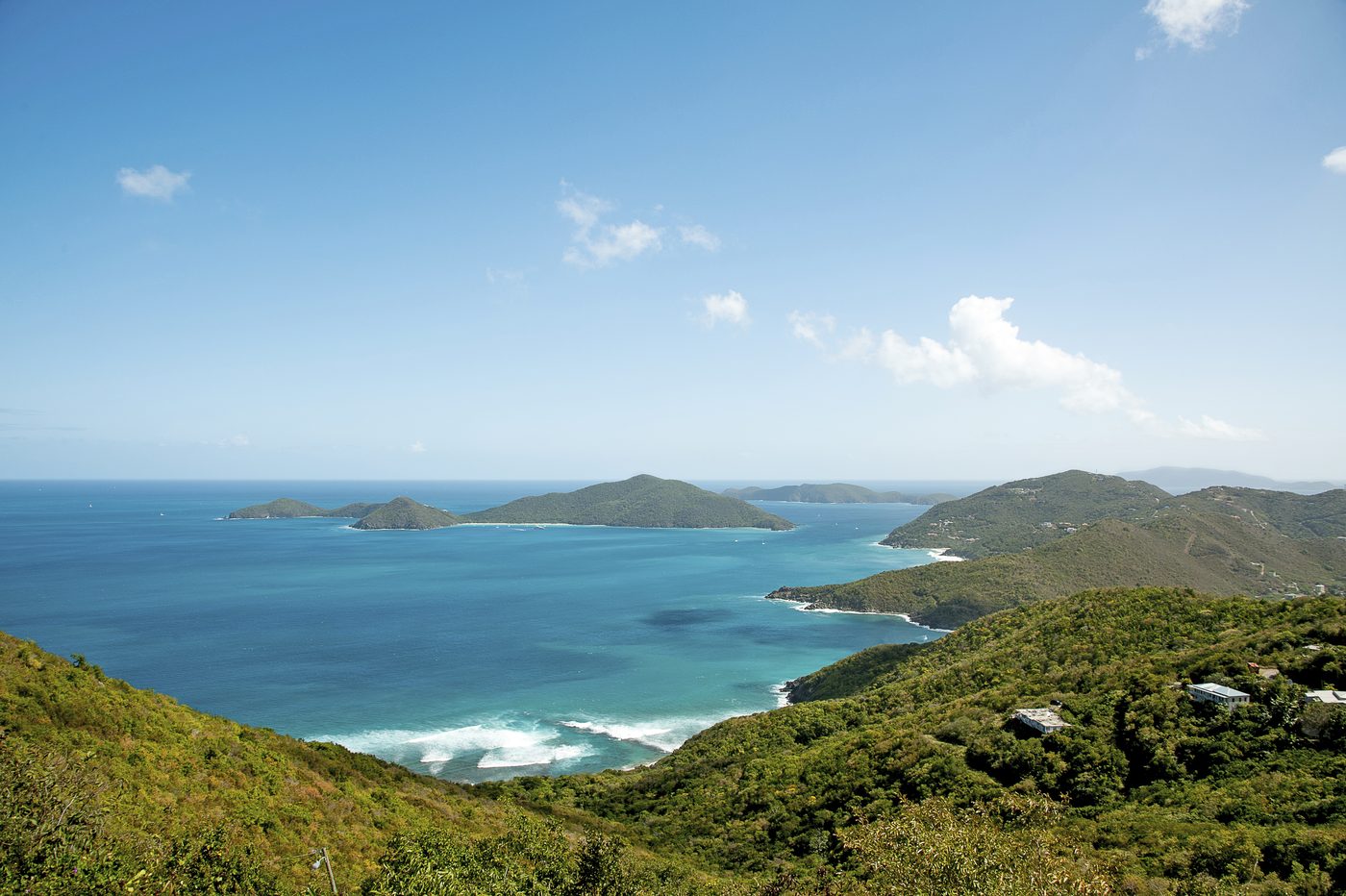 Blick von einer grünen Anhöhe über eine türkisblaue Bucht mit vorgelagerten grünen Inseln