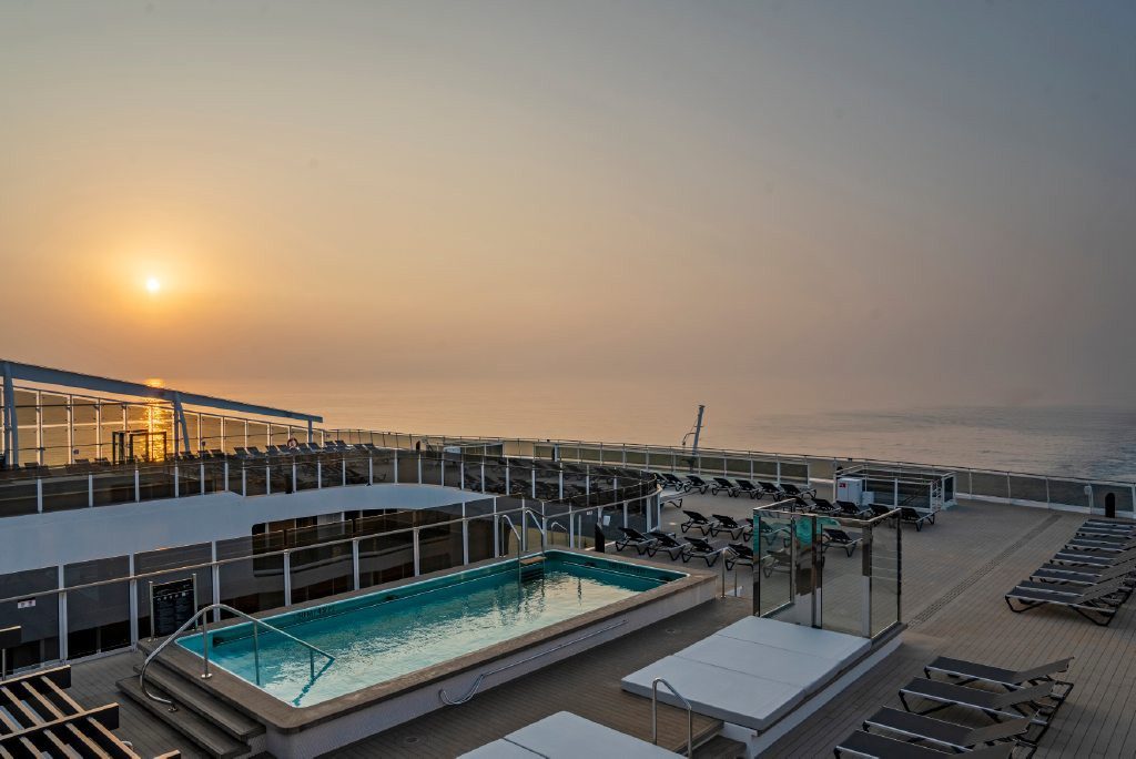 Pooldeck der MSC World Europa mit Pool und Sonnenliegen im Licht der aufgehenden Sonne