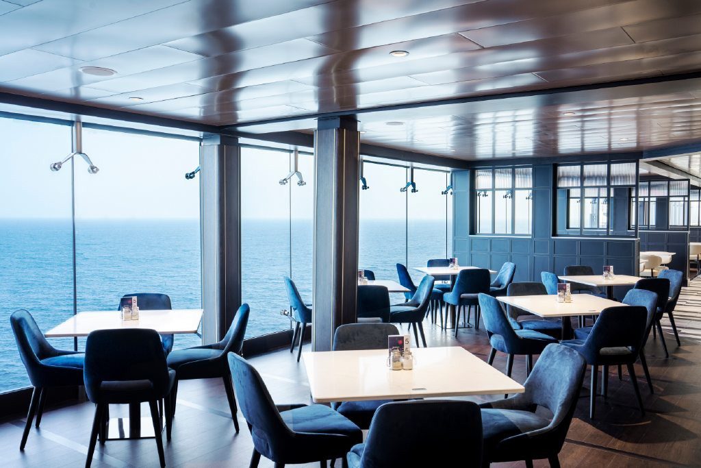 Restaurant mit blauen Sesseln und bodentiefer Fensterfront mit Blick aufs Meer
